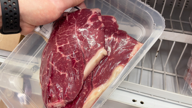 A hand taking a packet of steaks out of the fridge