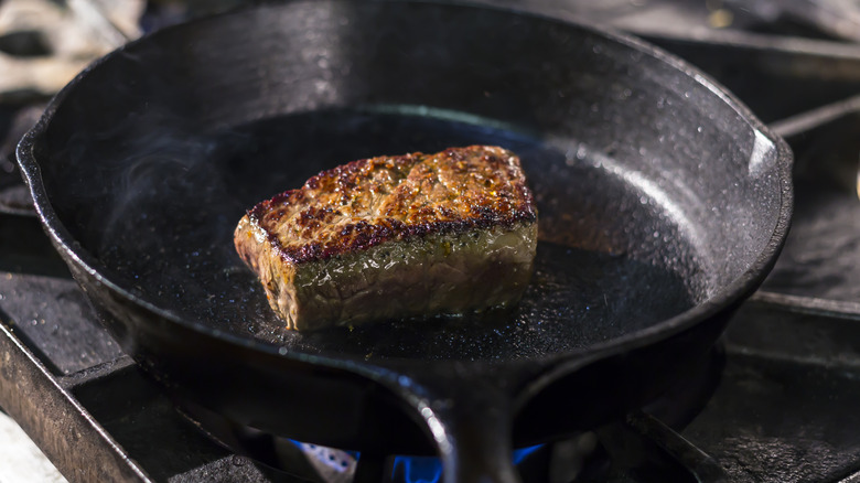 A steak sizzling while cooking in a cast-iron skillet