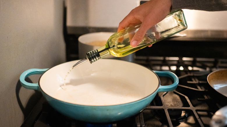 A hand adding oil into a pan on the stove