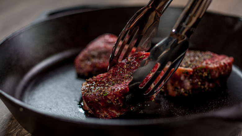 Tongs placing some pieces of tenderloin in a cast-iron pan