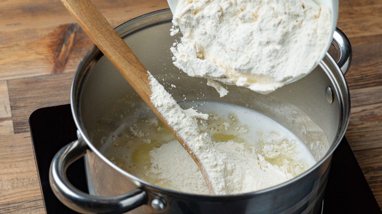 Flour being poured into pot of milk
