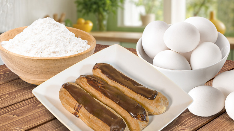 three chocolate eclairs on plate surrounded by eggs and flour