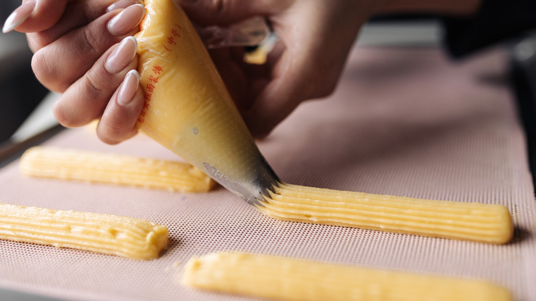 Person piping eclairs onto baking sheet
