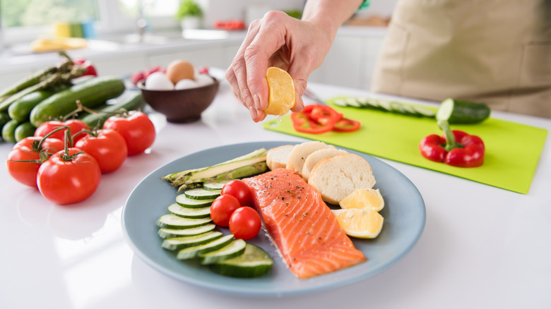 A hand squeezes lemon on salmon