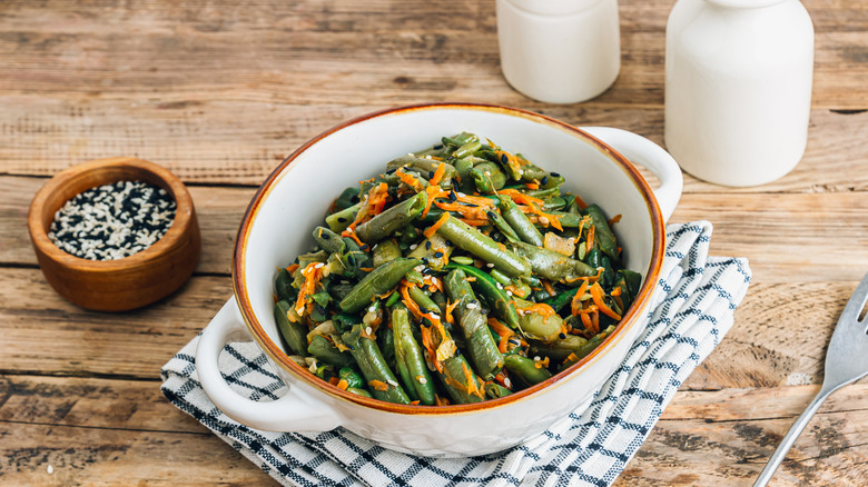 Green bean slaw in bowl on wooden table next to sesame seeds