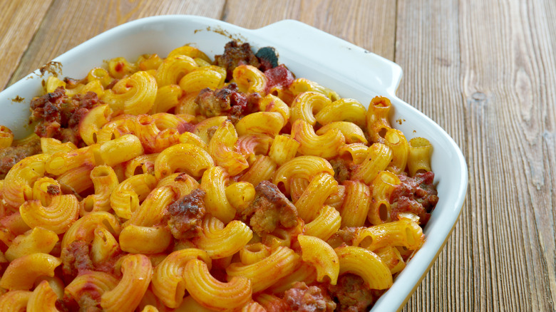 A macaroni casserole with bits of ground beef and tomato visible inside a white casserole dish on a wooden table top