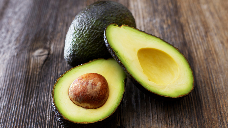 1 whole and 1 halved avocado on wooden surface