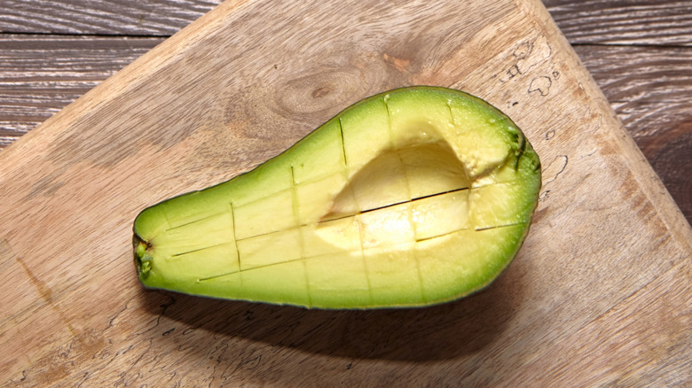 half an avocado on a cutting board with grid pattern cut into the flesh