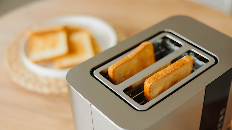 Two pieces of toast in a silver toaster with more toast out of focus in the background