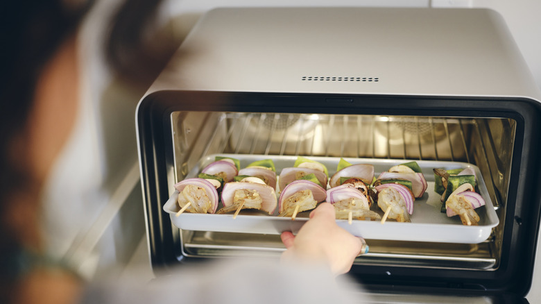 Person cooking kebabs in a toaster oven