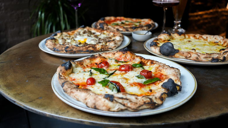 Four small pizzas on a table. The pizzas have fluffy, doughy crusts with large, charred air bubbles around their edges