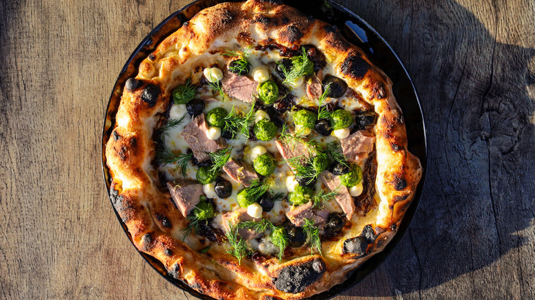 A Neapolitan pizza on a wooden table, topped with brussels sprouts and herbs