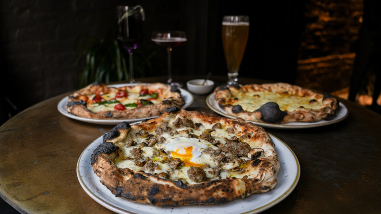 Three Tokyo-style Neapolitan pizzas on plates with various glasses of beer behind them