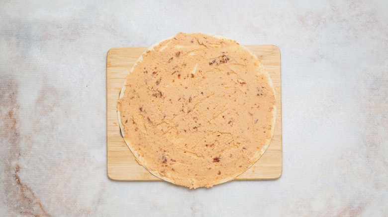 Hummus spread onto tortilla on wooden board