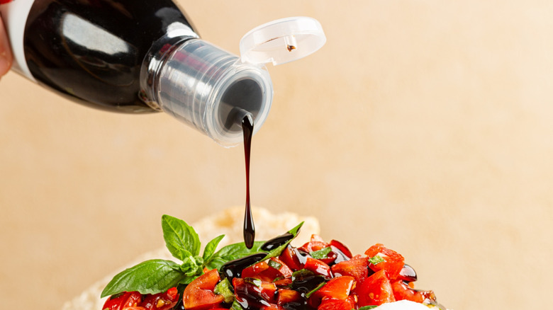 Balsamic glaze being poured over a tomato salad