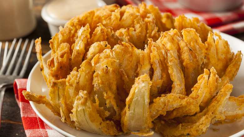 a Bloomin' Onion on a plate with napkins, cutlery, and a ramekin of sauce beside it