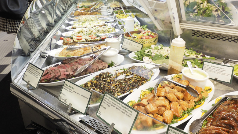 The prepared food case in a grocery tore has salmon, roast beef, and different salads.