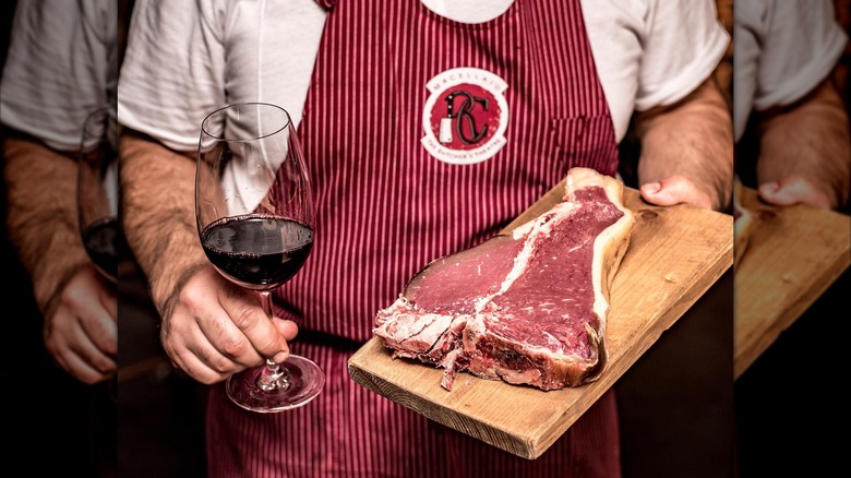 man holding steak and glass of wine