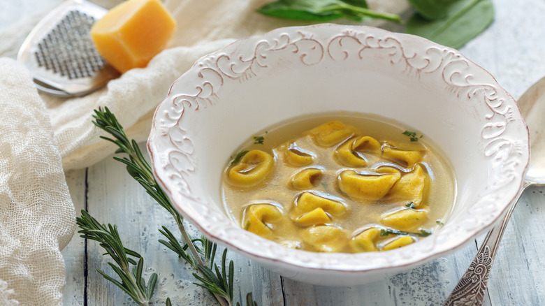 Tortellini soup and herbs in white bowl