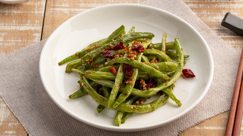 a plate of fried green beans topped with dried chilies
