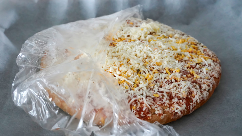 Frozen pizza halfway removed from its plastic wrapping on a grey surface