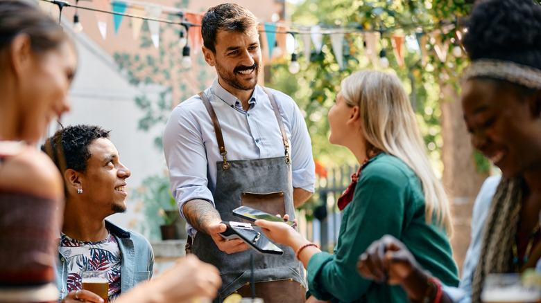 A waiter helping customers pay their bill at an outdoor restaurant