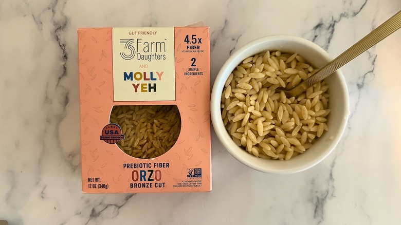 Package of 3 Farm Daughters and Molly Yeh orzo next to small cup of orzo with spoon, all on marble surface