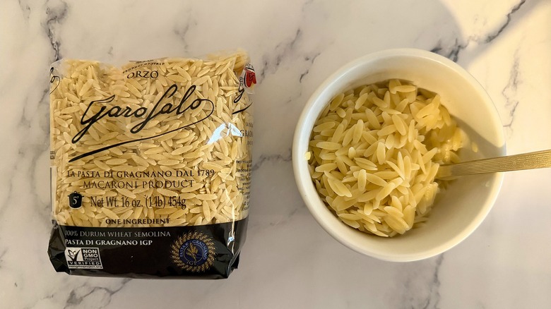 Package of Garofalo orzo next to small cup of orzo with spoon, all on marble surface