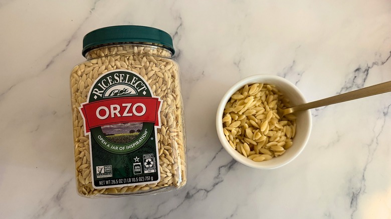 Package of Rice Select orzo next to small cup of orzo with spoon, all on marble surface