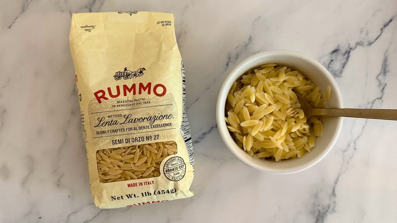 Package of Rummo orzo next to small cup of orzo with spoon, all on marble surface