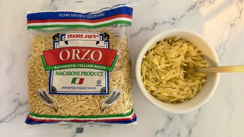 Package of Trader Joe's orzo next to small cup of orzo with spoon, all on marble surface
