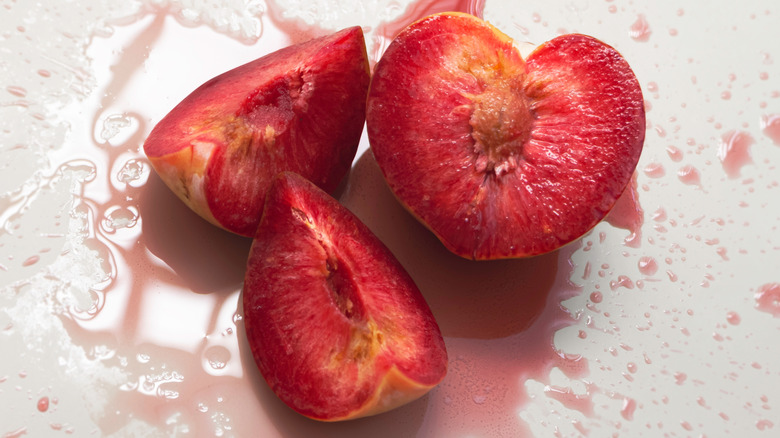Plumcot sliced open, with splash of liquid on surface underneath.