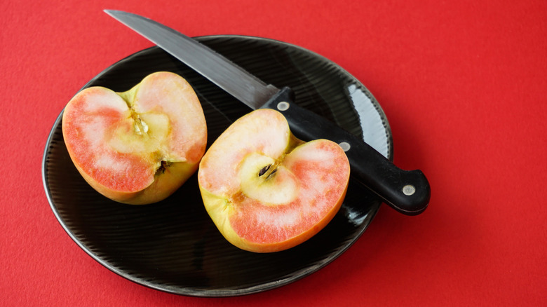Lucy Glo apple sliced in half on plate with knife.