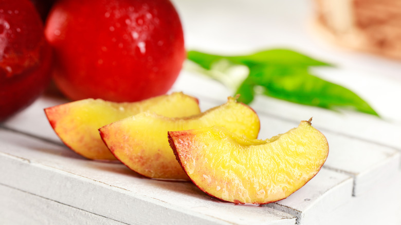Nectarine slices on wooden pallet next to whole fruits.