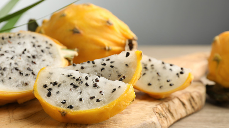 Yellow dragon fruits on wooden cutting board, one sliced to show flesh inside.