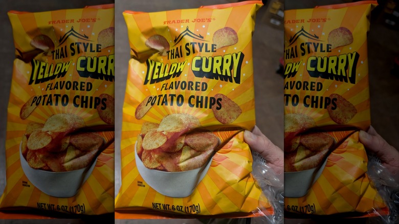 hand holds bright yellow striped bag of Trader Joe's Thai Style yellow curry chips