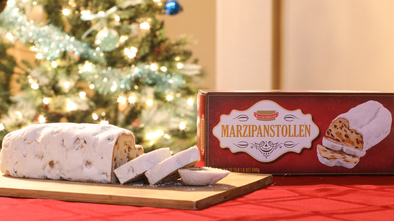 A loaf of KuchenMeister Marzipan Stollen sliced on a table in front of a Christmas tree