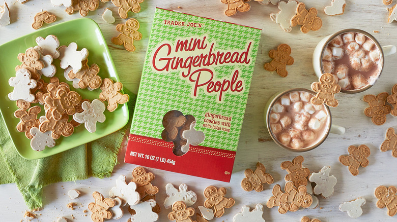 A green plate of Trader Joe's Mini Gingerbread People on a table next to mugs of cocoa and a box of the cookies