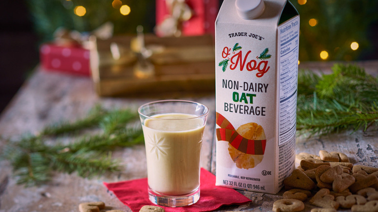 A glass of Trader Joe's O'Nog Non-Dairy Oat Beverage on a festive holiday table next to a carton of the beverage