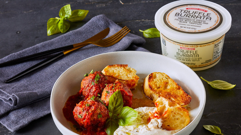 Trader Joe's Truffle Burrata on a table next to a white plate of appetizers, including meatballs and garlic bread