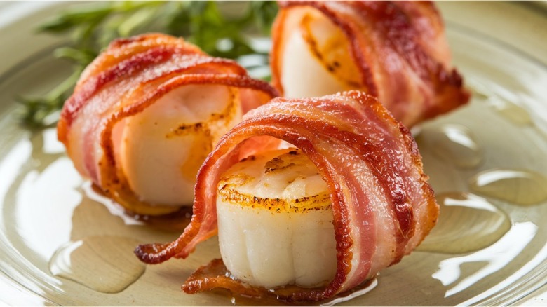 A close-up of three bacon-wrapped scallops on a glass plate