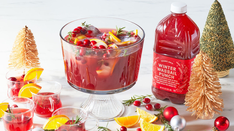A glass punch bowl containing Trader Joe's Winter Wassail Punch garnished with cranberries, lemon, and rosemary