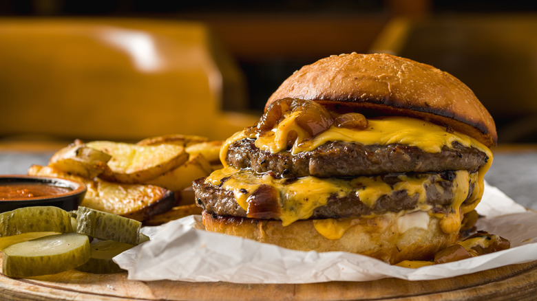 cheeseburger on wood board with pickles and fries