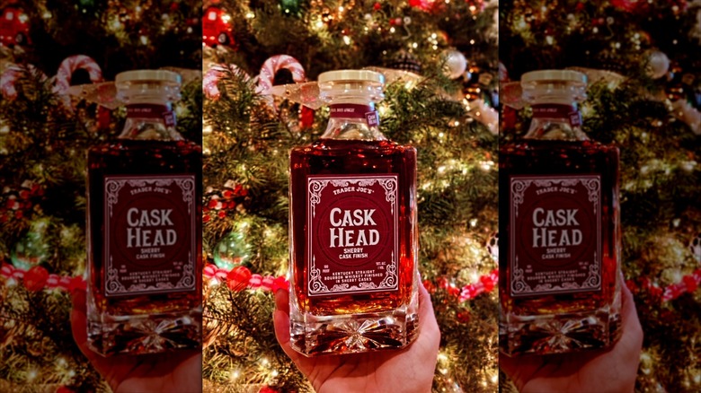 A hand holding bottle of Trader Joe's new Cask Head Sherry Cask Finish bourbon up in front of a tree
