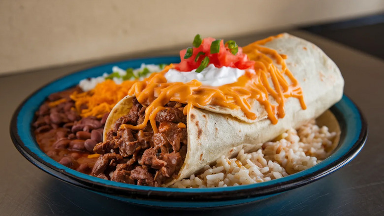 burrito with cheese and tomatoes on rice and beans