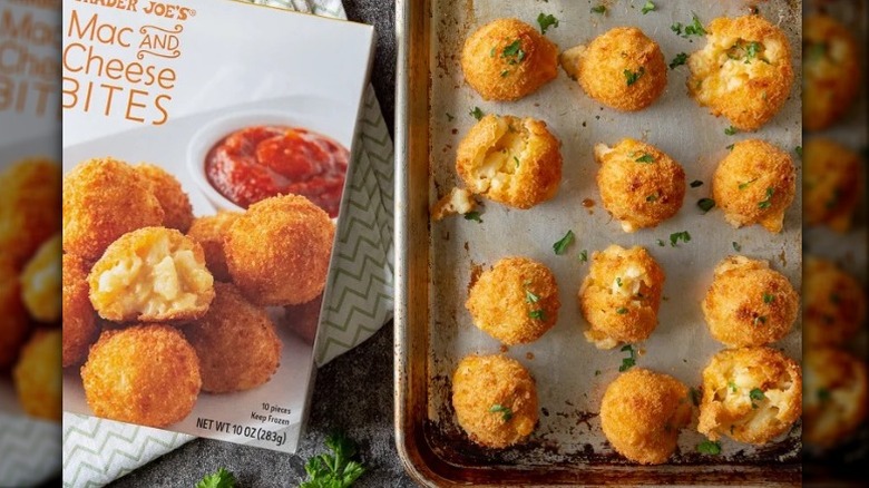 A box of Trader Joe's mac and cheese bites box sitting beside a baking pan covered in hot mac and cheese bites.