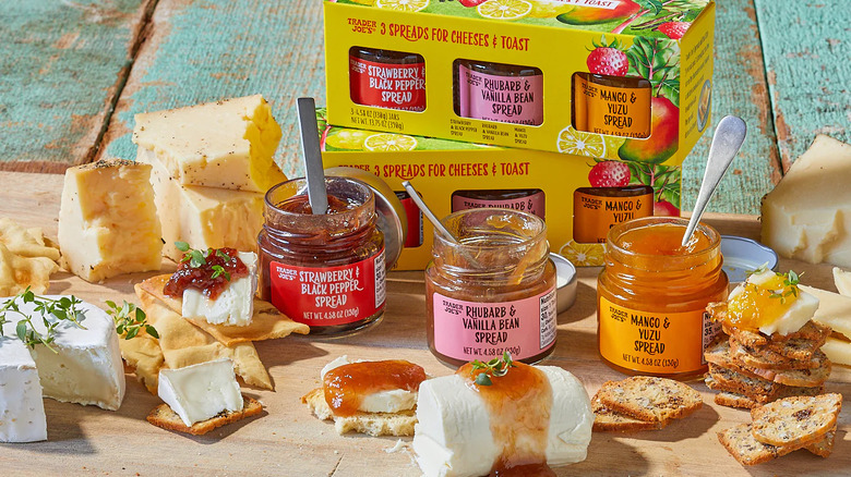 Two packages of Trader Joe's 3 Spreads for Cheeses & Toast surrounded by bread and cheese topped with the spreads