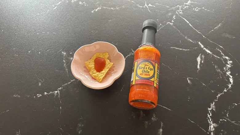 A bottle of Trader Joe's Bird's Eye Chile Hot Sauce on a kitchen counter next to a chip with hot sauce on it