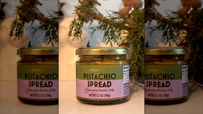 A jar of Trader Joe's Pistachio Spread on a table in front of a fir tree