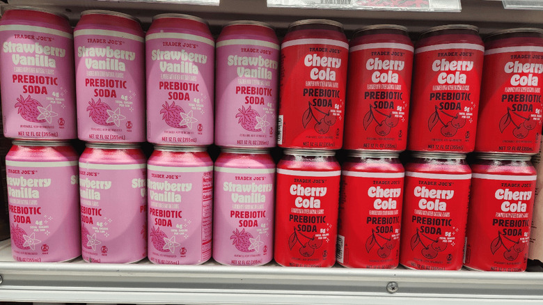 Cans of Trader Joe's Strawberry Vanilla and Cherry Cola Prebiotic sodas on a store shelf
